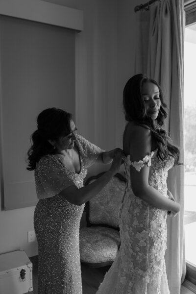 Mother of bride zipping up her daughters wedding dress, in black and white.