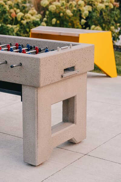 An outdoor foosball table in front of a bright yellow chair and flowery bushes