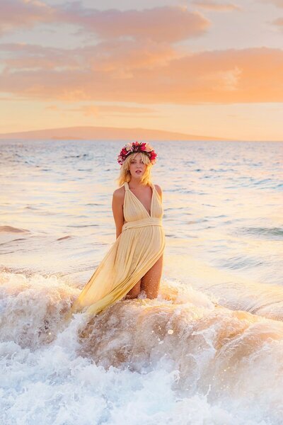 pregnant woman in gold kasia kulenty gown poses on the beach at sunset with love and water