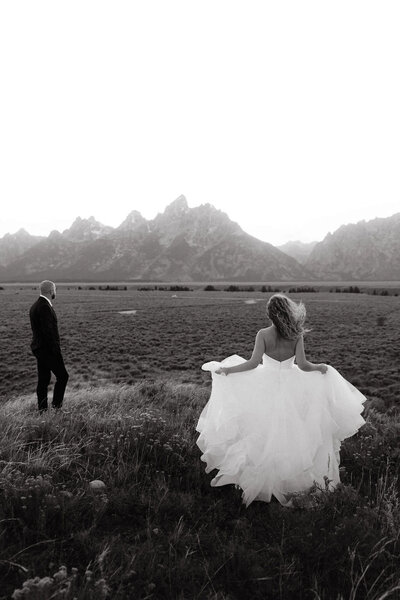 bride running across an open field to groom with mountains in the background