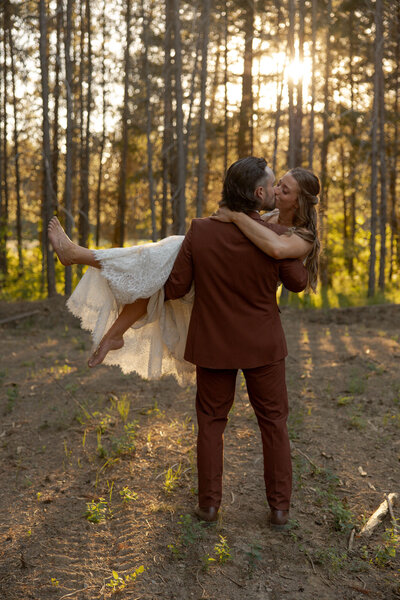 Groom holding bride and walking through the woods taken by Boise wedding photographer.