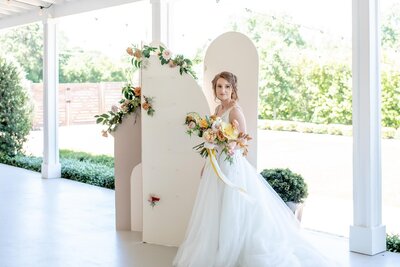 Bride standing in front of a neutral colored custom arch backdrop design