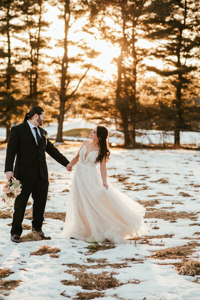 A bride and groom holding hands while standing in a snowy, wooded area.