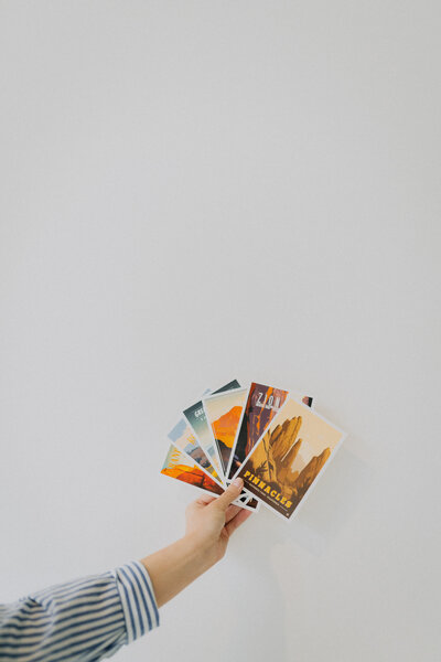Hand holding up travel postcards in front of a white wall