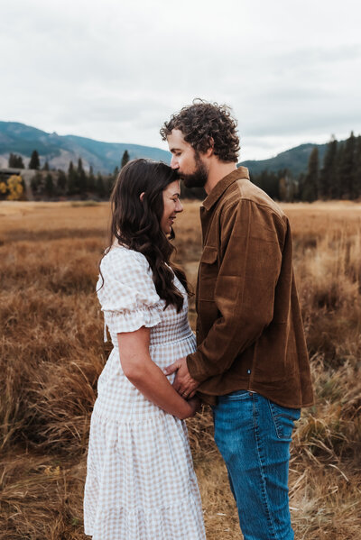 A husband kisses his expecting wife on the forehead while holding her pregnant belly.