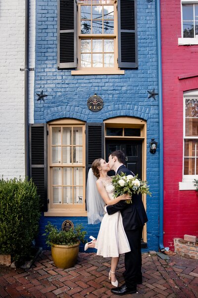 a bride and groom kiss in front of a tiny house in old town alexandria