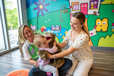 Female business owner of Hartbeeps in Westport, CT, is holding a cat puppet while the cat is giving a little girl a hug.