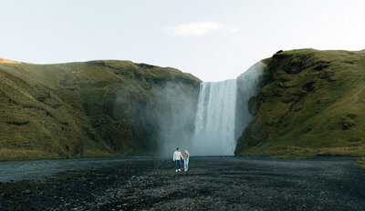 Couple standing at the base of a waterfall in Iceland, captured by a destination elopement photographer.