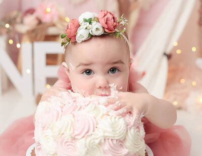 A delightful girl playfully smashing her face into a delicious cake during a cake smash photography session in Rochester, NY. The colorful frosting and vibrant decorations add a fun atmosphere to the moment.