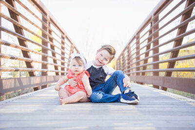 A brother and sister pose for a sweet picture to celebrate the sister's one year milestone on a park bridge  as captured by las vegas wedding and portrait photographer, Jessica Bowles
