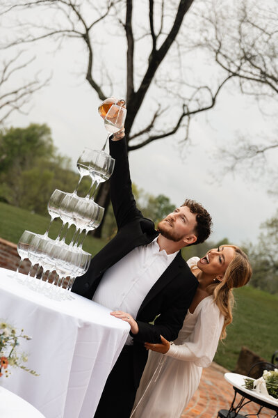 Bride and groom pouring champagne into a tower at their Kentucky wedding, capturing a joyful and celebratory moment of their day.