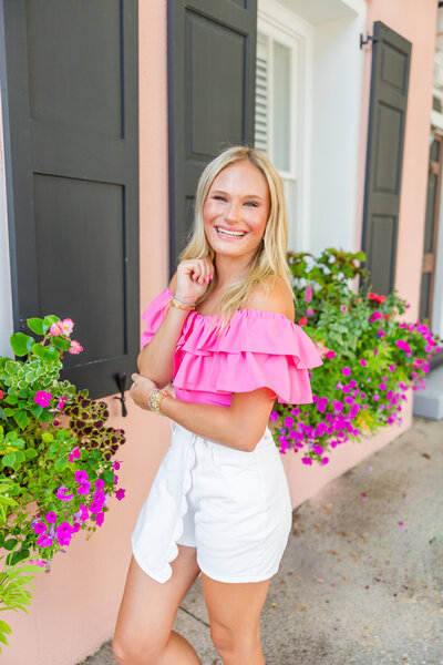 blonde haired high school girl with blonde hair and hot pink shirt on with white shorts and florals in the background in Charleston, South Carolina