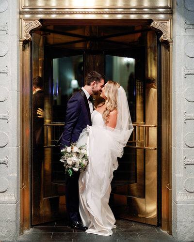 Newlyweds share a joyful moment exiting a downtown Pittsburgh hotel with romantic evening light and celebration energy.
