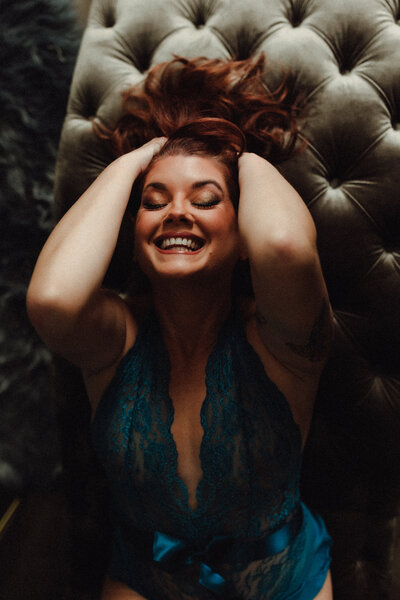 Woman laughing and lying on wood floor during black and white boudoir shoot in Gainesville, Florida studio.