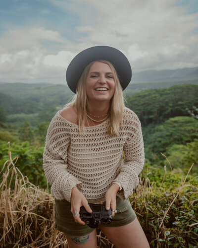 Big Sur Elopement Photographer holding a vintage film camera and smiling with potted plants in the background