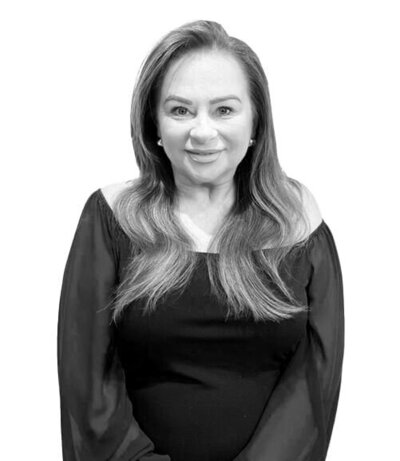Smiling female Art Director with long wavy hair in an off-shoulder black top, representing expertise as a Salon Manager and Makeup Artist.