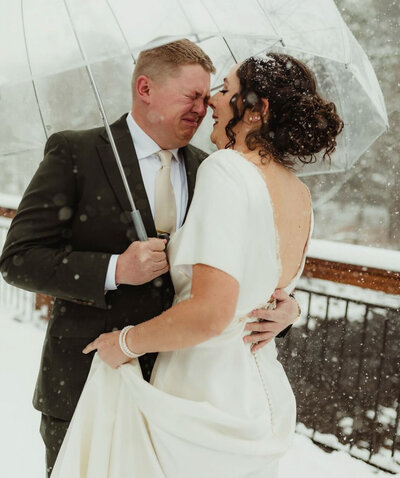 Couple embracing under an umbrella in the snow on their wedding day