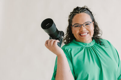 A photographer with a camera in one hand and a smile on her face