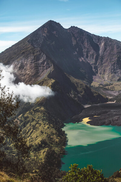 Volcanic mountain and turquoise crater lake with misty clouds drifting past.