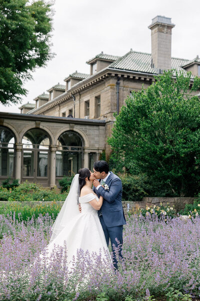 Contact | Newport and CT Wedding Photography & Videography | Light and Airy | Couple kissing with a mansion behind them in front of lavender bush.