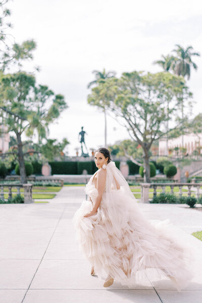 bride in an off white, semi pink ruffled gown running away from the camera and looking back over her shoulder