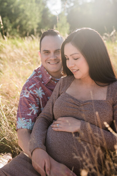 Couple sitting in golden field at sunset for outdoor maternity photos at Fort Steilacoom park