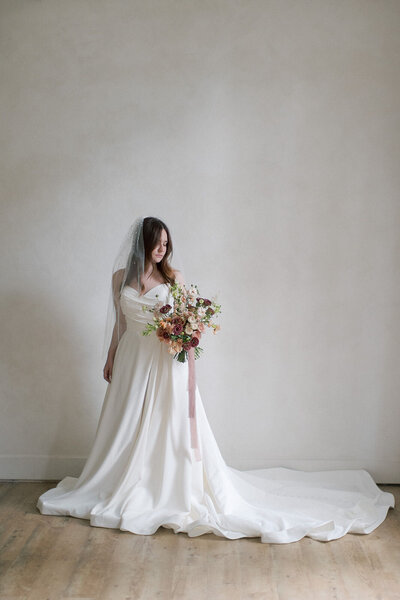 A bride in her wedding dress and veil holding a large bouquet 