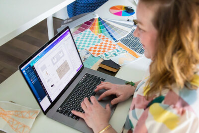 Woman on laptop with color swatches and pattern samples on desk