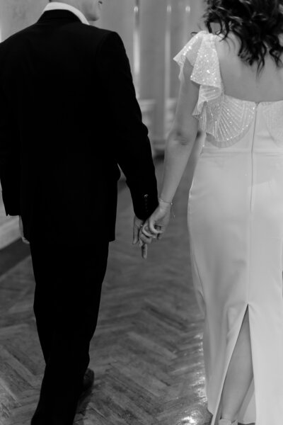 black and white view of bride and groom holding hands and walking away together