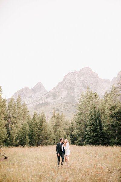 bride and groom walking through a field after their grand teton elopement taken by photographer adrian wayment photo