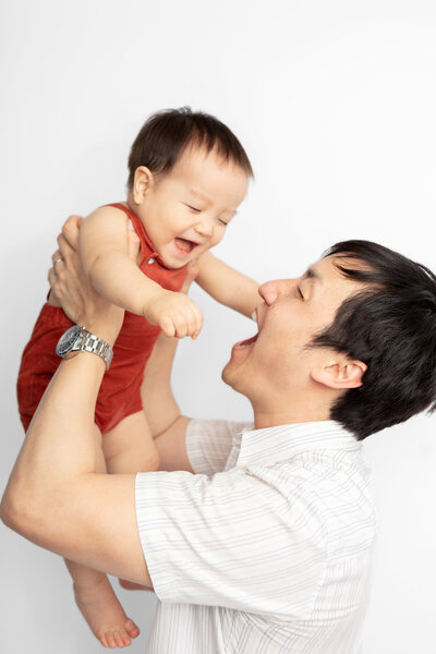 family studio session with laughing dad holding up giggling baby boy