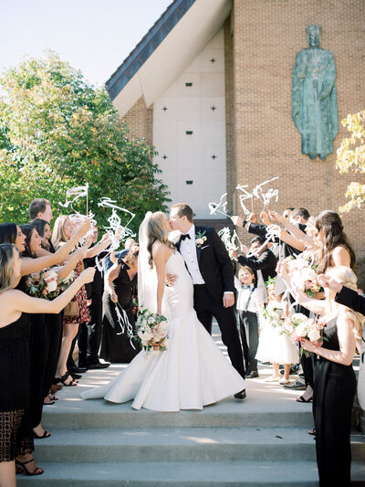 Bride and groom kissing in front of a church as they walk away from their wedding ceremony.