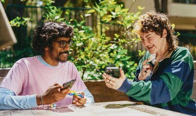 Two people smiling at a phone screen. Photo by Hiki App on Unsplash.