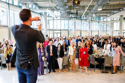 A man holding a phone taking a large group photo with his camera.