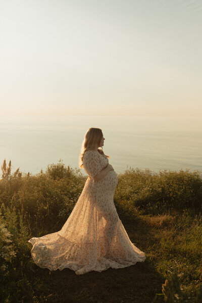 woman holding baby bump in front of ocean for lifestyle photos at prince edward island