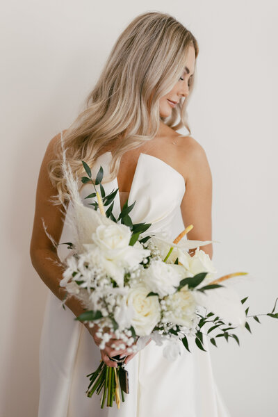bride wearing her wedding dress and holding bridal bouquet while gently smiling