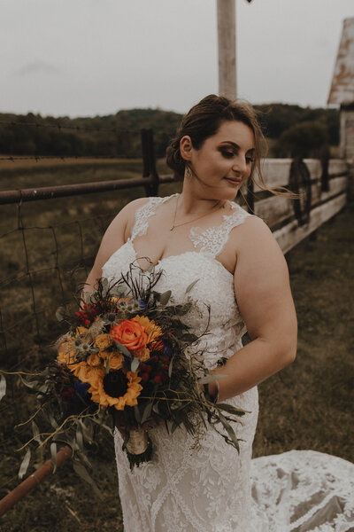Bride standing with bouquet looking away from camera in autumn 