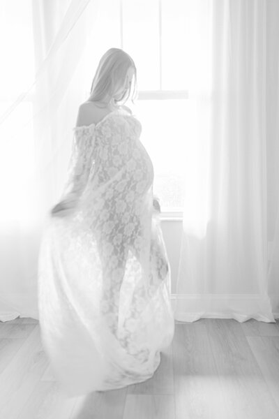 Elegant Tampa maternity portrait of mother-to-be in lace gown dancing in front of window in natural light studio session