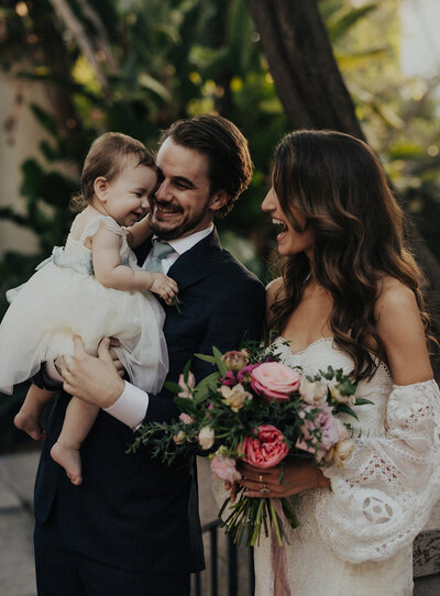 Moody and Romantic Wedding Portrait. A smiling groom picks up and twirls his beautiful bride in front of a bougainvillea bush.