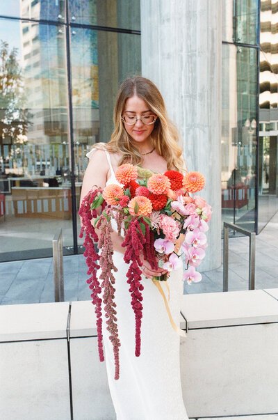 Bride poses in front of Multnomah County Courthouse with her bouquet for a photograph after her wedding.