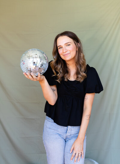 A freelance branding and website designer poses with a disco ball.