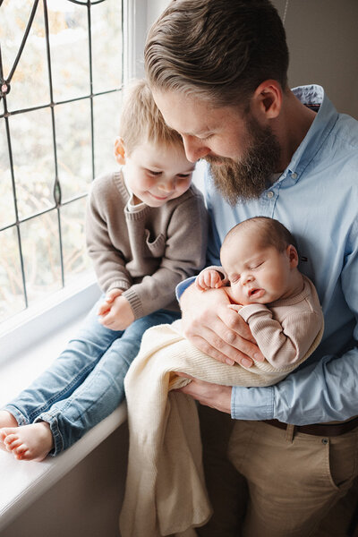 dad holding newborn with toddler