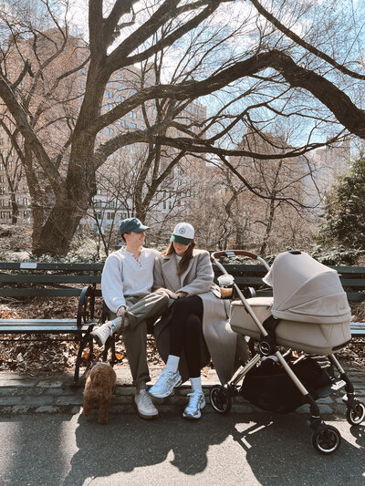 Anna and Nathan page sitting on an NYC bench with a strolling and their dog