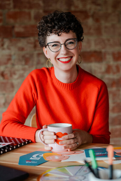 Wedding planner in bright orange sweater with cup of coffee, smiling