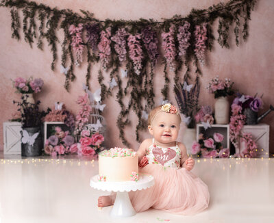one year old girl in pink dress  with floral backdrop for cake smash photoshoot