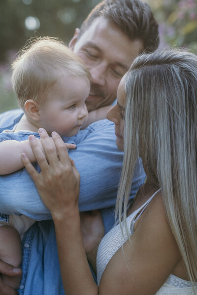 Dad holds baby, which is looking at her mom.