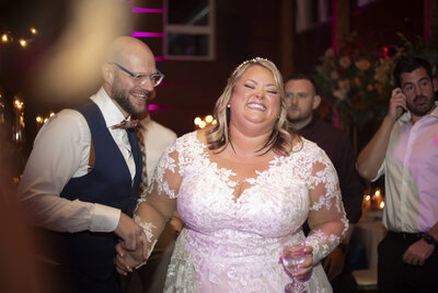 A newlywed couple laughing as one of them holds a drink 