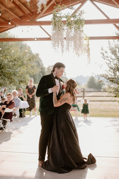 A Cannon Beach Wedding Photographer image of Newlyweds in a black dress and tux dancing under market lights at their outdoor venue