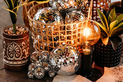Detail shot of boho disco styled elopement decor. It features a basket of disco balls, faux plants, and a glowing Edison bulb.