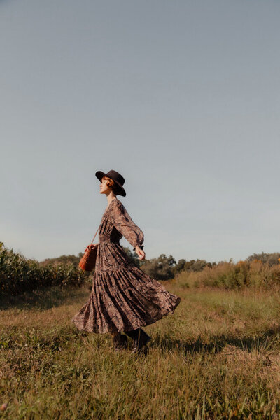 a woman wearing a dress dancing in a field at sunset
